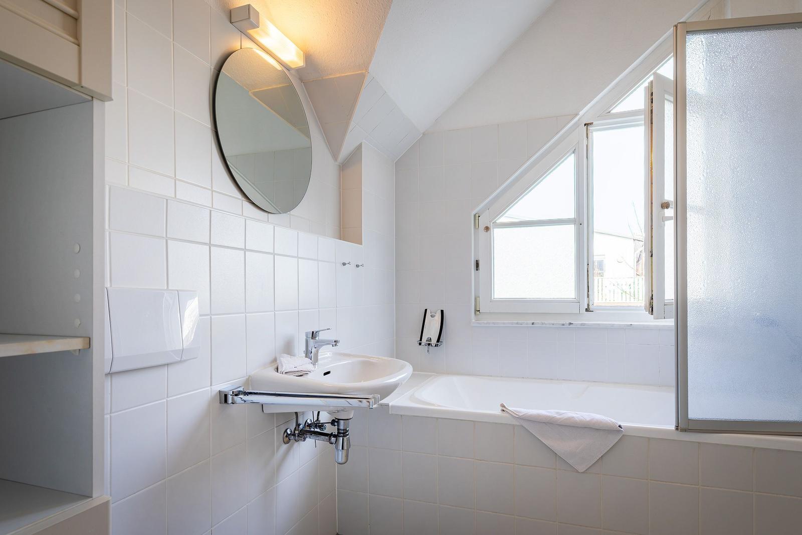 Badezimmer mit Badewanne, Waschbecken und Duschabtrennung. Fenster mit Blick nach draußen.