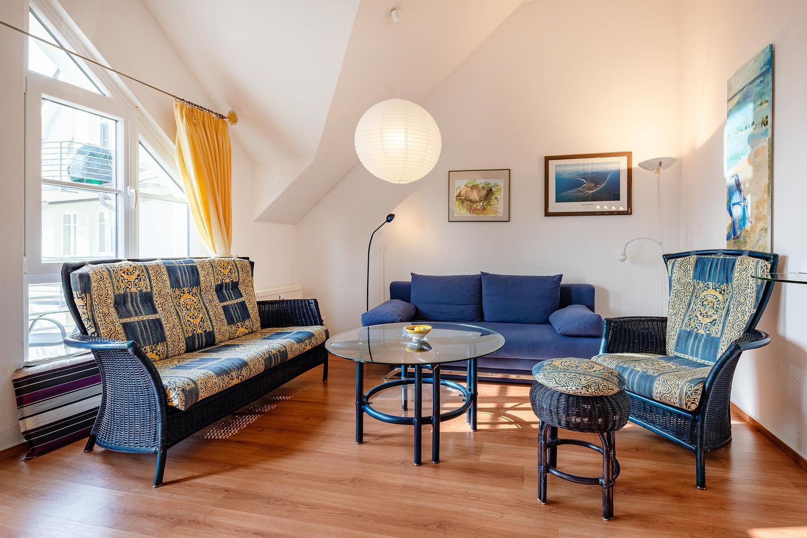 Wohnzimmer mit Sitzgruppe, Glas-Tisch und Fenster. Decke geneigt, Holzboden.
