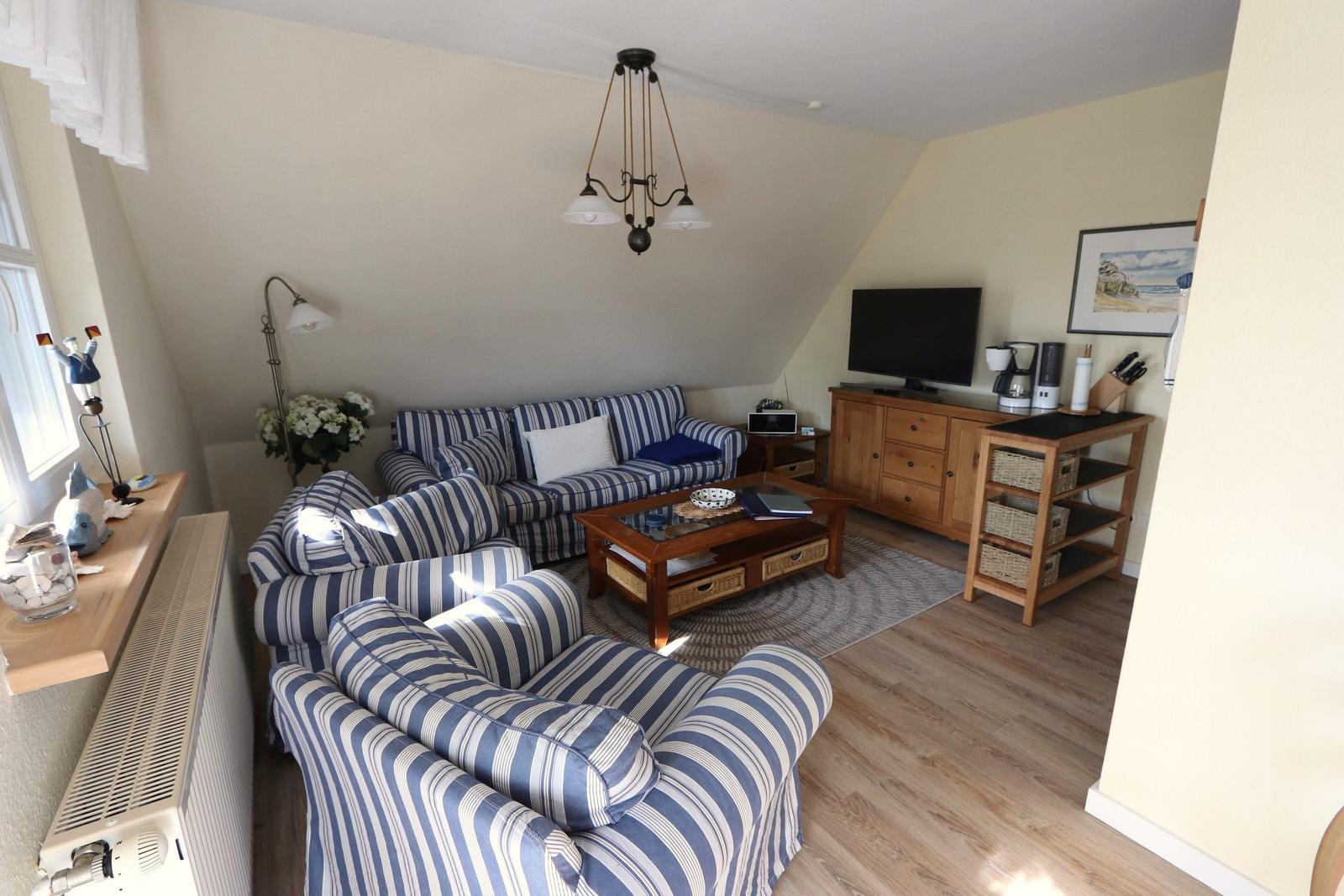 Wohnzimmer mit Sofa, Sessel und Fernseher. Holzmöbel und Streifenbezüge.