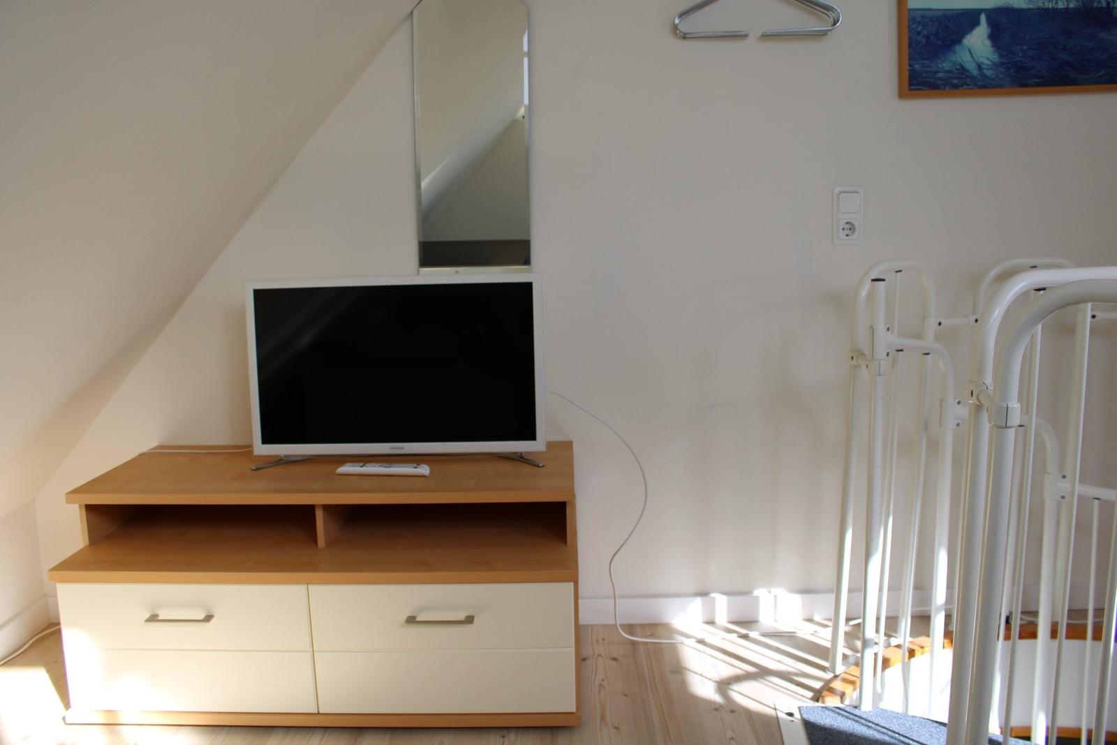 TV auf Holzregal, Spiegel an der Wand, weißer Kleiderständer und Bild