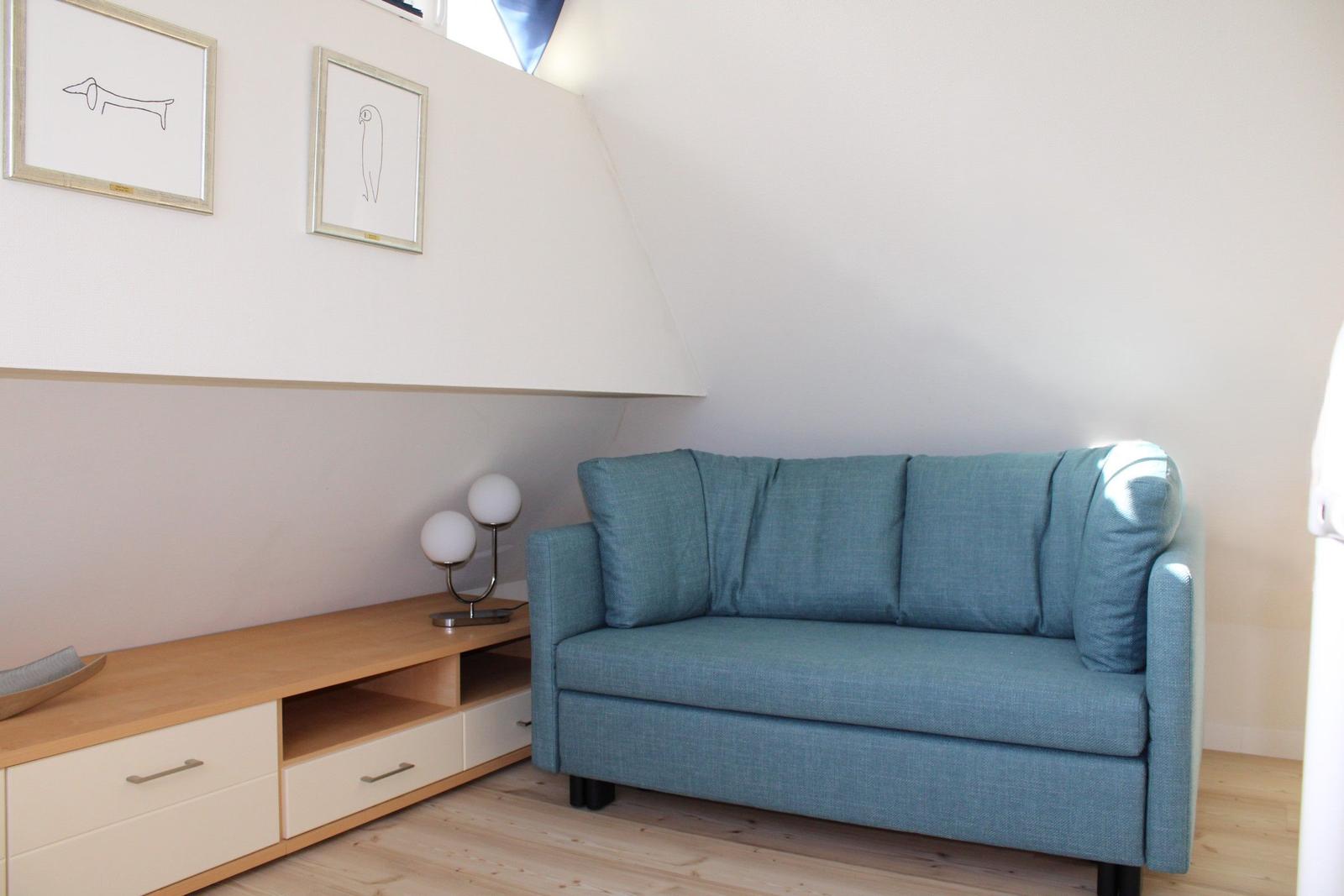 Ein blaues Sofa steht neben einem Holzschrank mit Schubladen und einer Lampe.