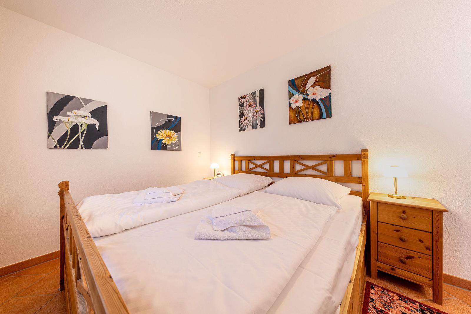 Schlafzimmer mit Holzbett, Nachttisch und Wandbildern