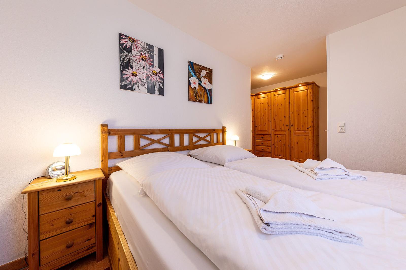 Ein Schlafzimmer mit Doppelbett, Holzmöbeln und zwei Wandbildern mit Blumenmotiven.