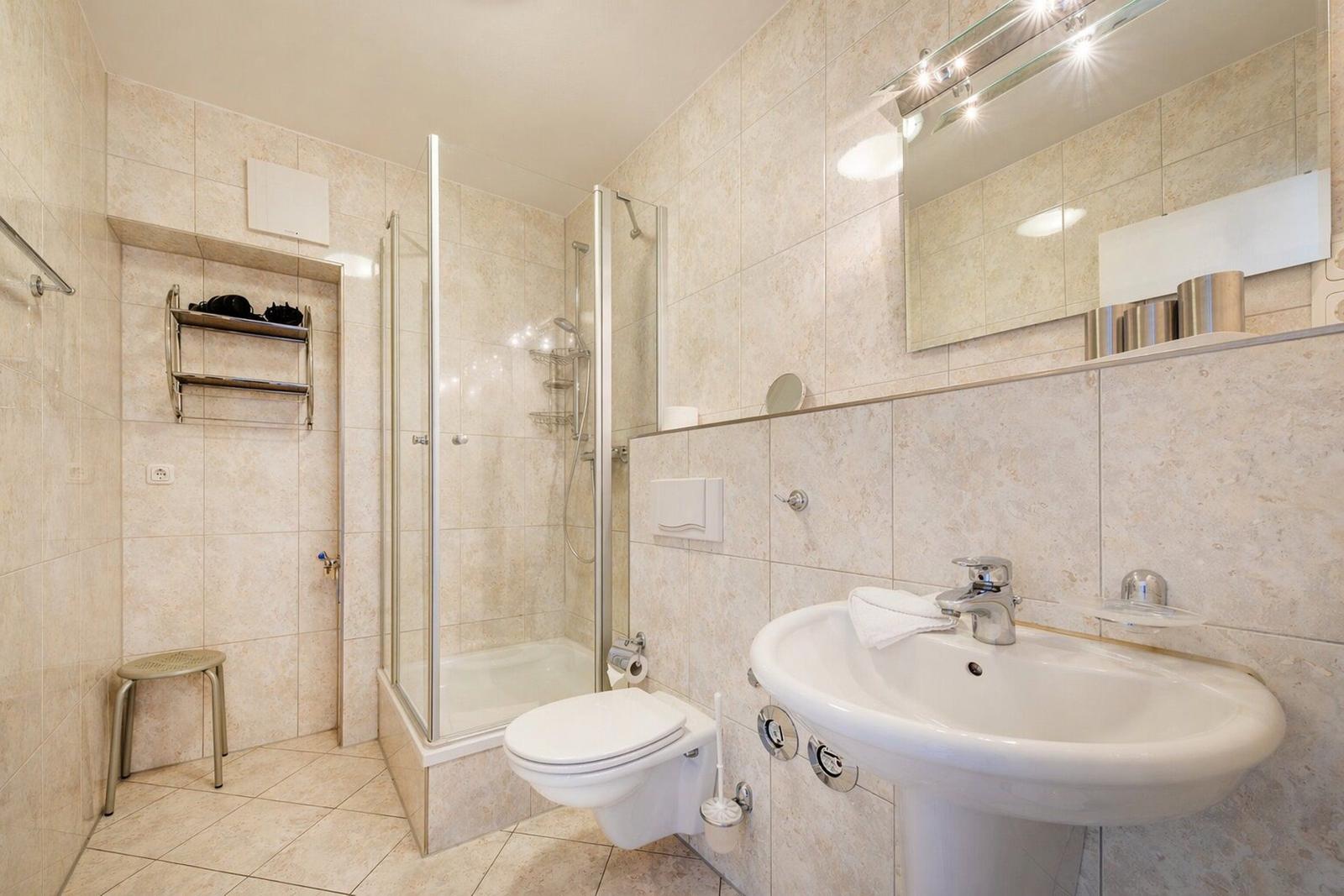 Badezimmer mit Dusche, Waschbecken und Toilette. Fliesenwand und Spiegel.