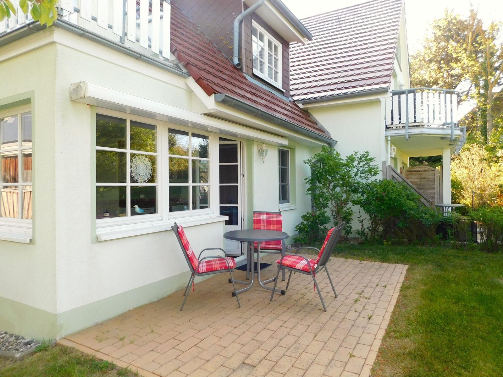 Haus mit Terrasse, Tisch und Stühlen mit karierten Sitzkissen.