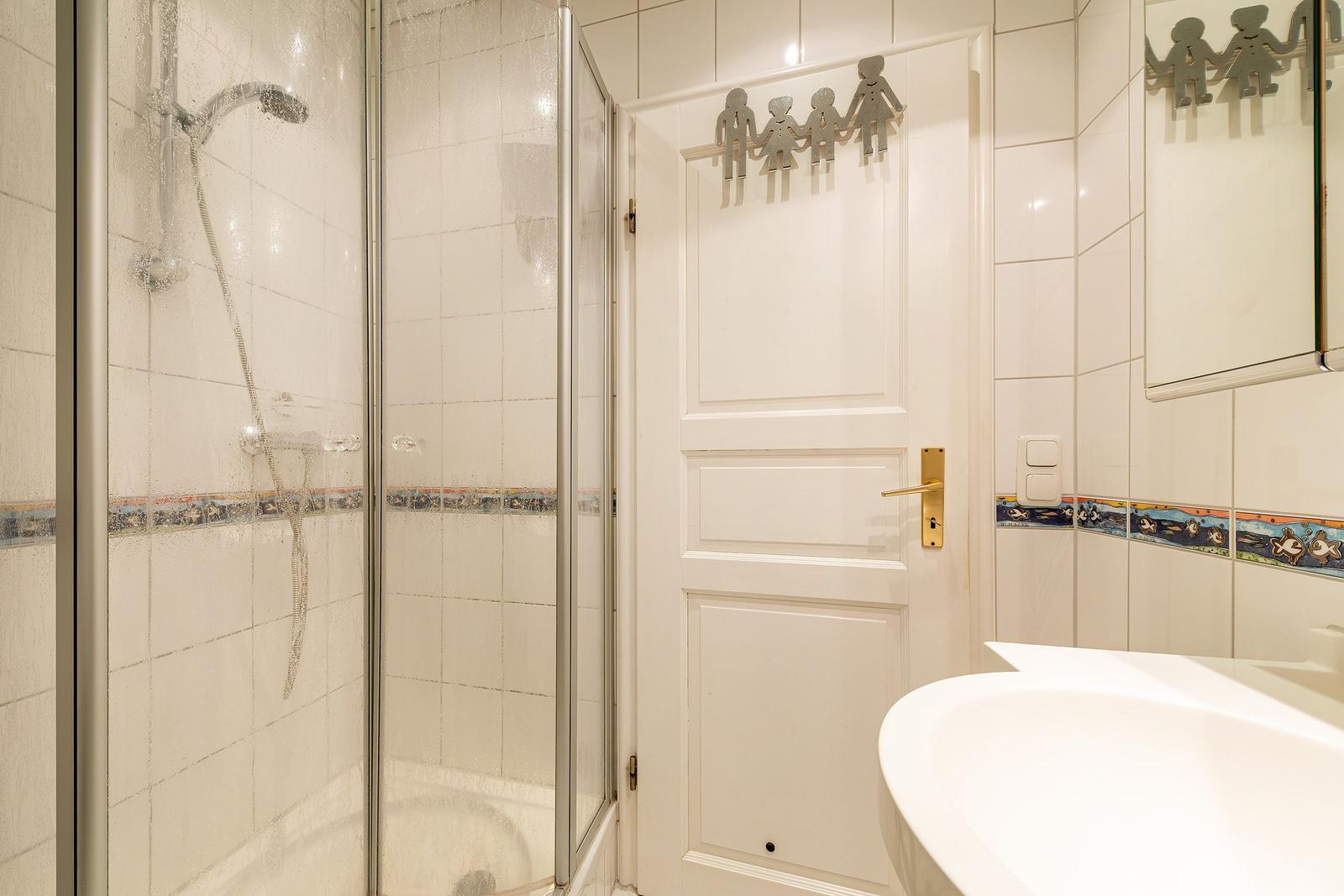 Badezimmer mit Dusche, Waschbecken und Tür mit Kinderdekoration.