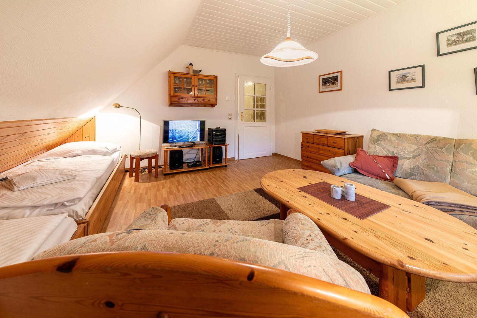 Ein Schlafzimmer mit Sofa, Holztisch und Fernseher in einem Dachzimmer.