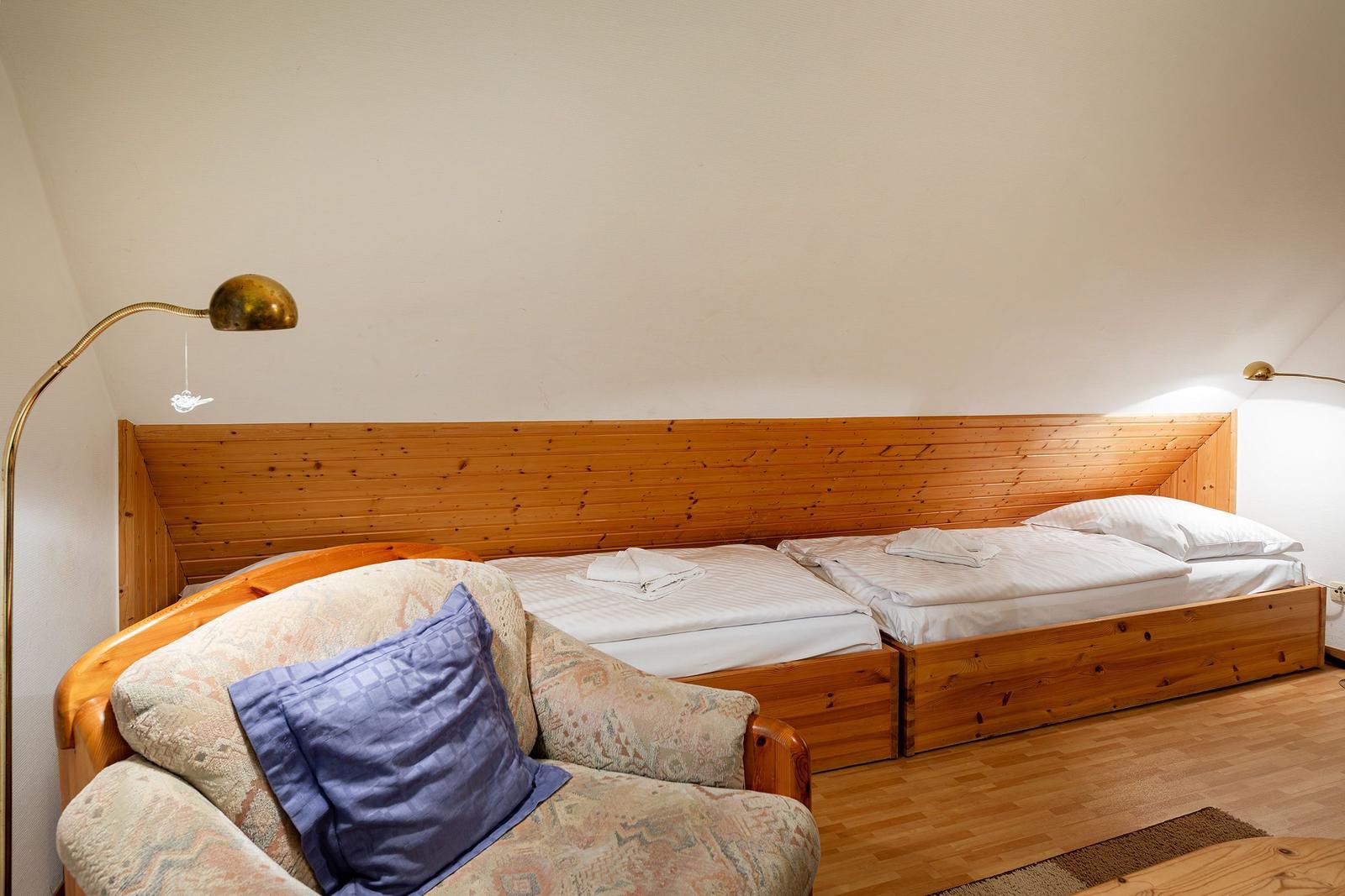 Zimmer mit zwei Betten, Holzrahmen und Sessel mit Kissen.