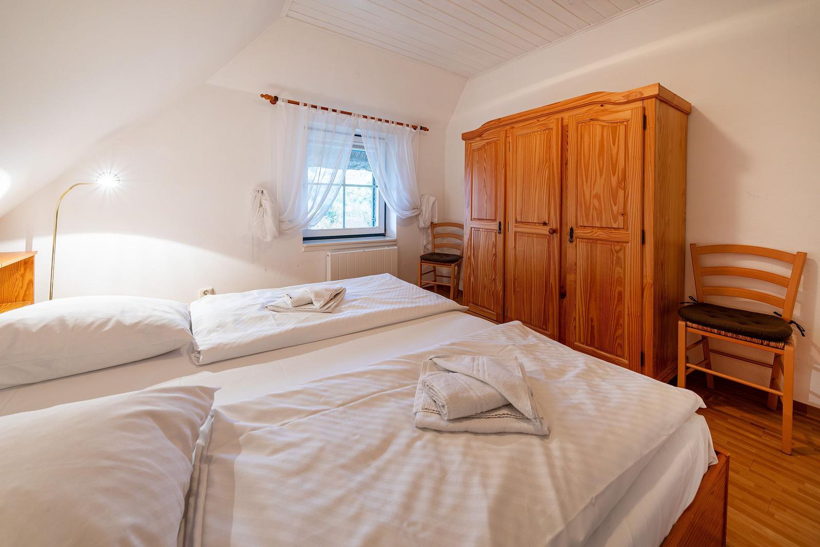 Schlafzimmer mit Doppelbett, Holzschrank und Fenster mit Vorhängen.