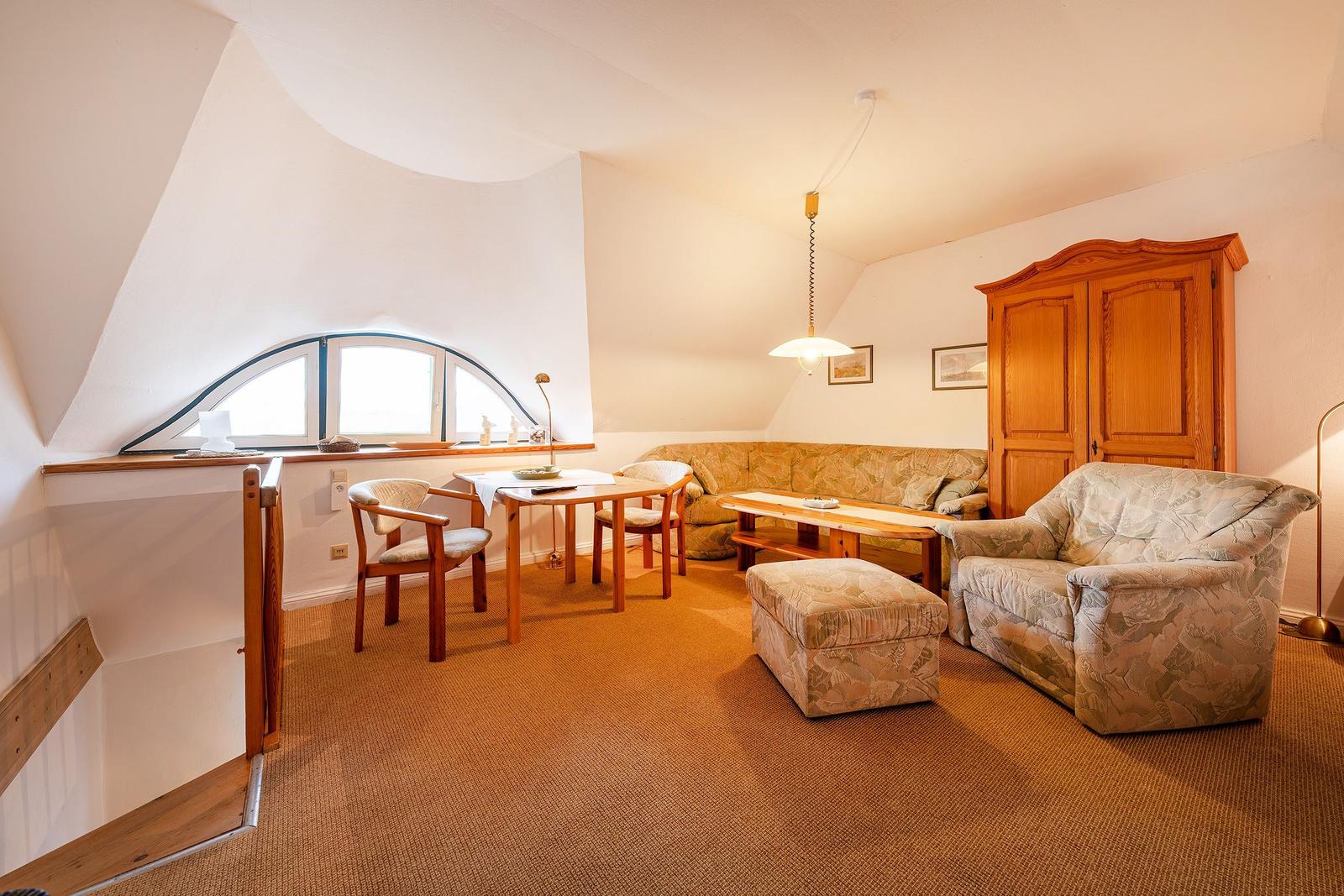 Wohnzimmer mit Sofa, Sessel, Tisch und Schrank unter schrägem Dach.