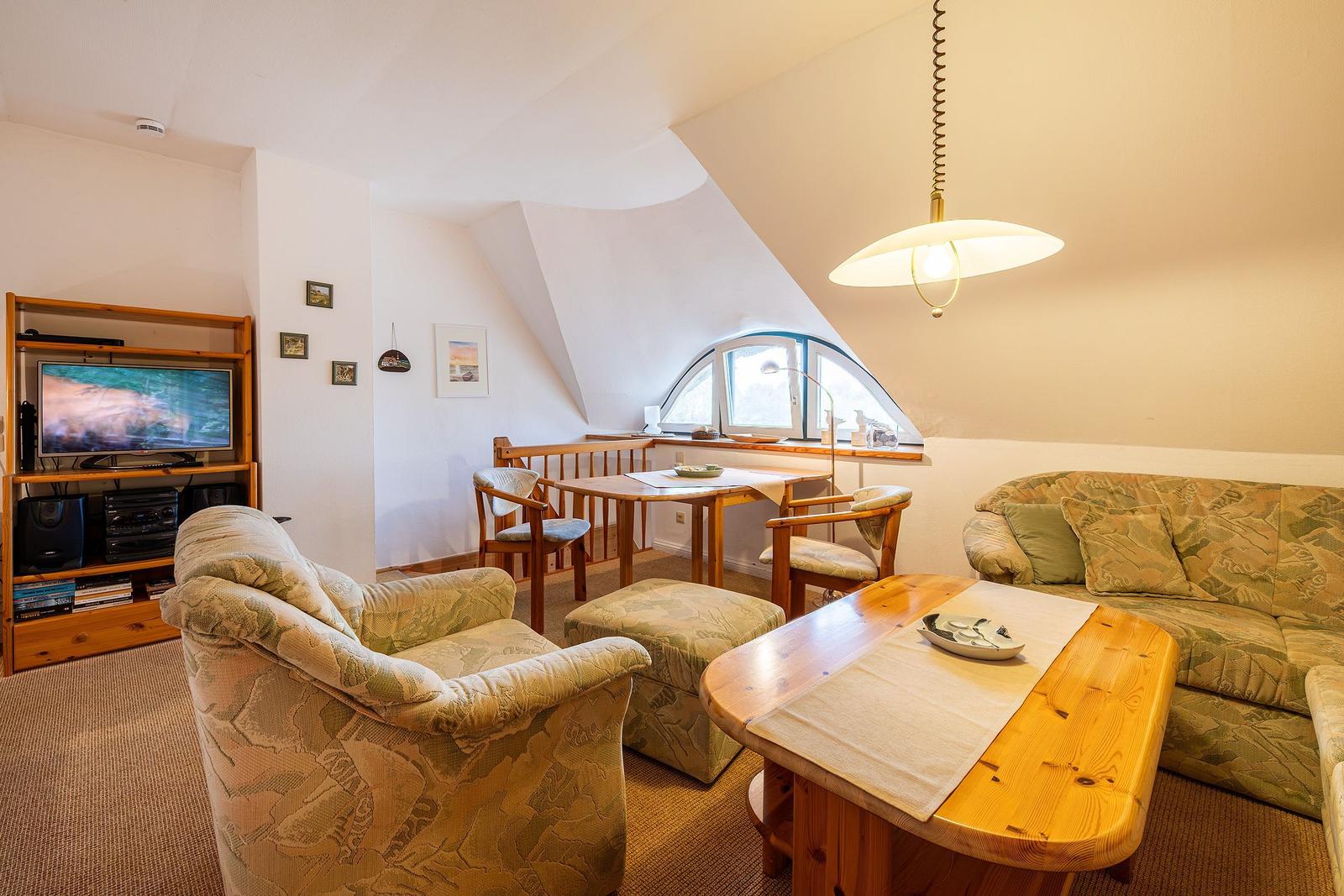 Wohnbereich mit Sofa, Sessel, Esstisch und TV-Möbel unter Dachschrägen.