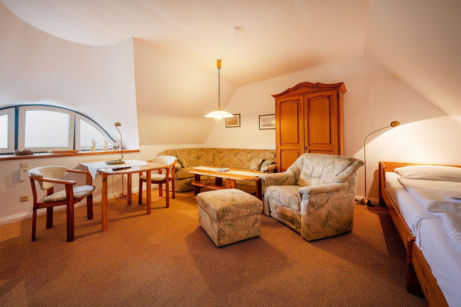 Ein Zimmer mit Bett, Sofa, Stuhl und Tisch unter einer geneigten Decke.
