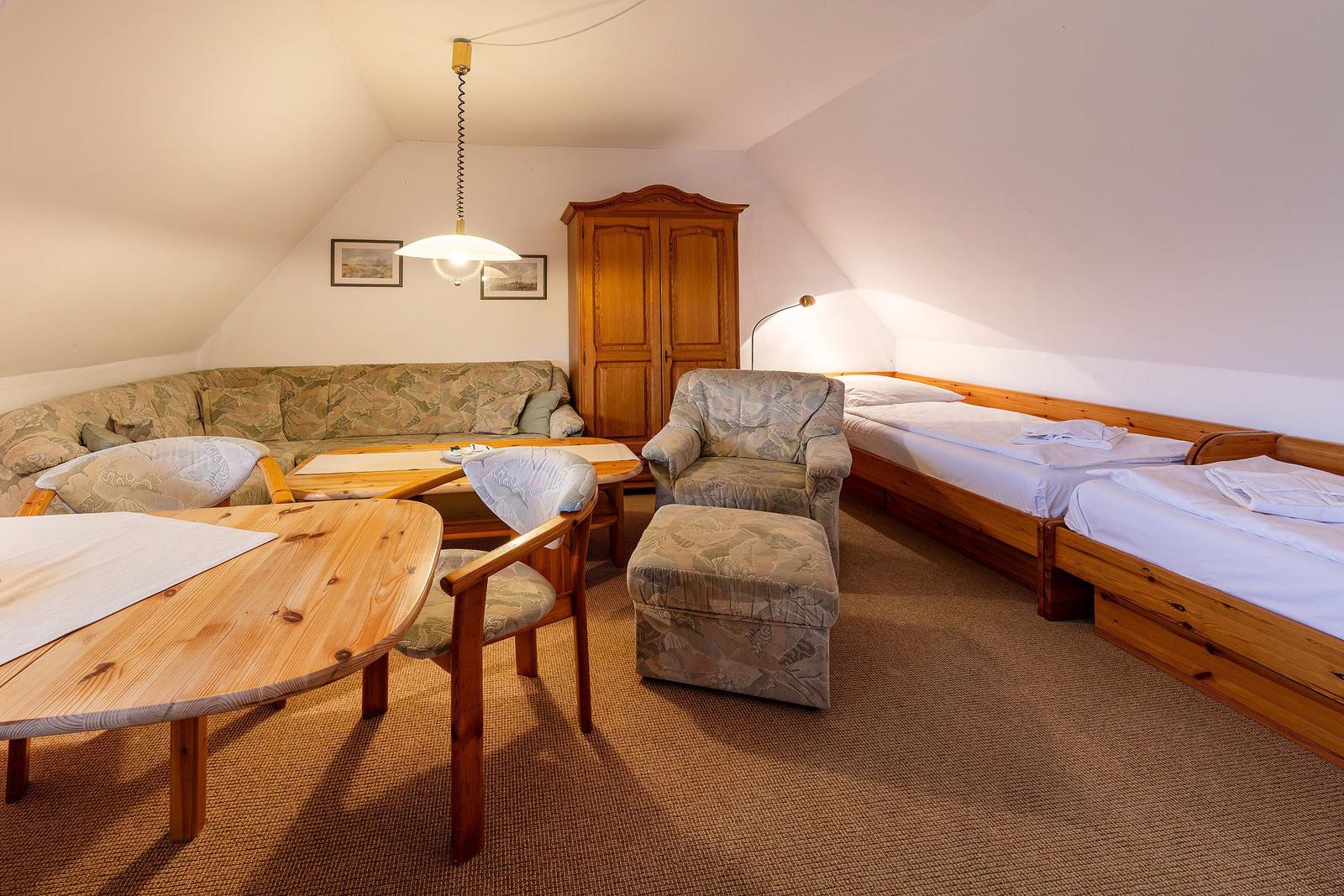 Zimmer mit zwei Betten, Sofa, Sessel und Holzmöbel.