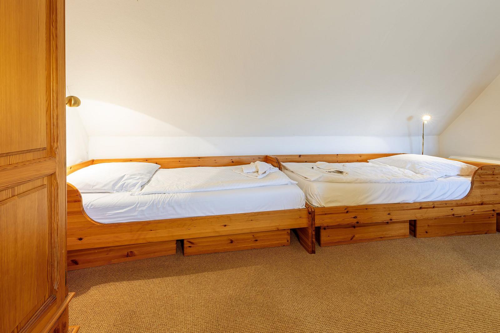 Zwei Holzbetten mit weißen Bettwäschen und Nachttischlampen in einem Dachzimmer.