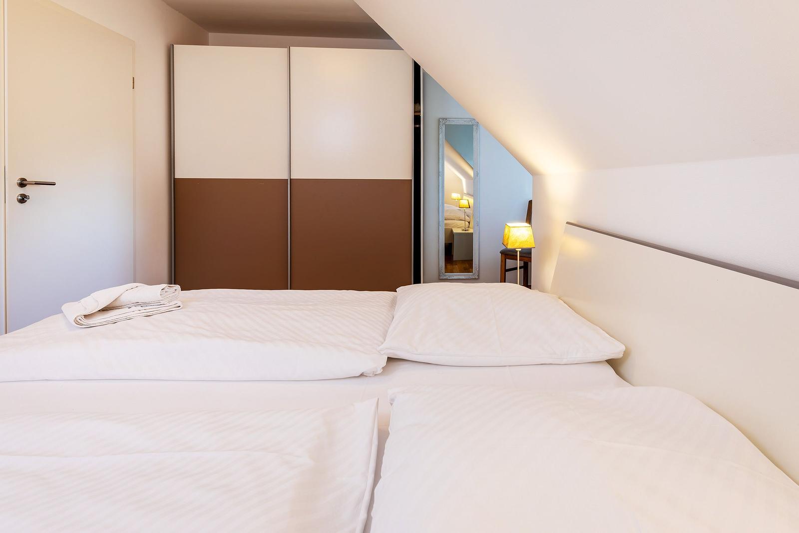 Schlafzimmer mit Doppelbett, Kleiderschrank und Spiegel an geneigtem Dach.