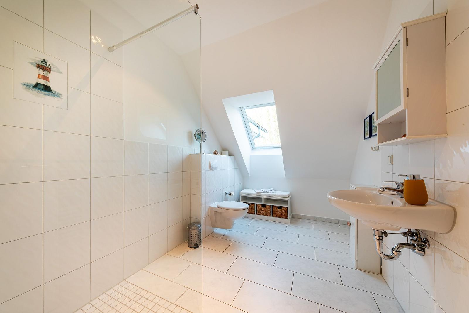 Badezimmer mit Dusche, WC und Waschbecken. Dachfenster und Wandbild mit Leuchtturm.