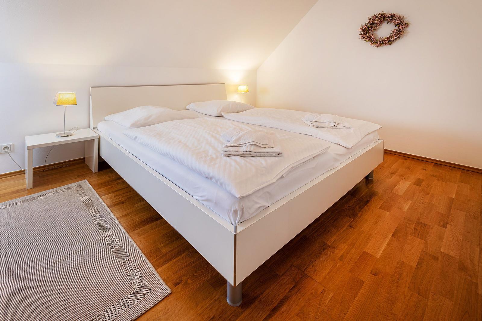 Schlafzimmer mit weißem Bett, Holzboden und Wandkranz.