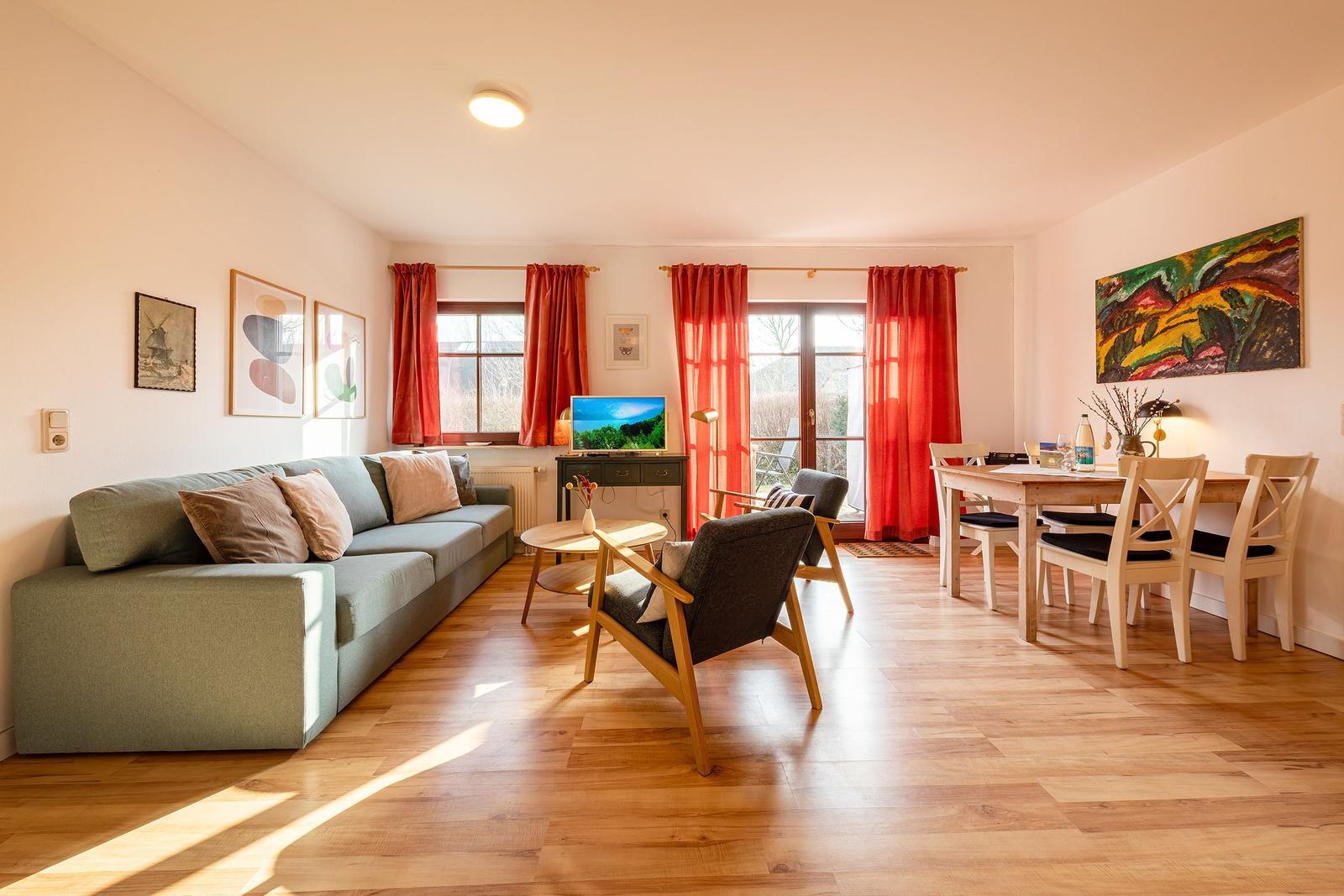 Wohn- und Essbereich mit Sofa, Stühlen, Tisch und roten Vorhängen.