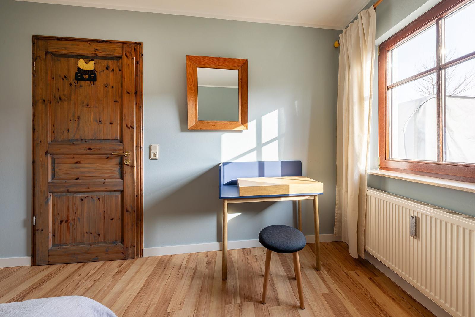 Ein Raum mit Holzboden, Holztür, Schreibtisch und Fenster mit Vorhang.