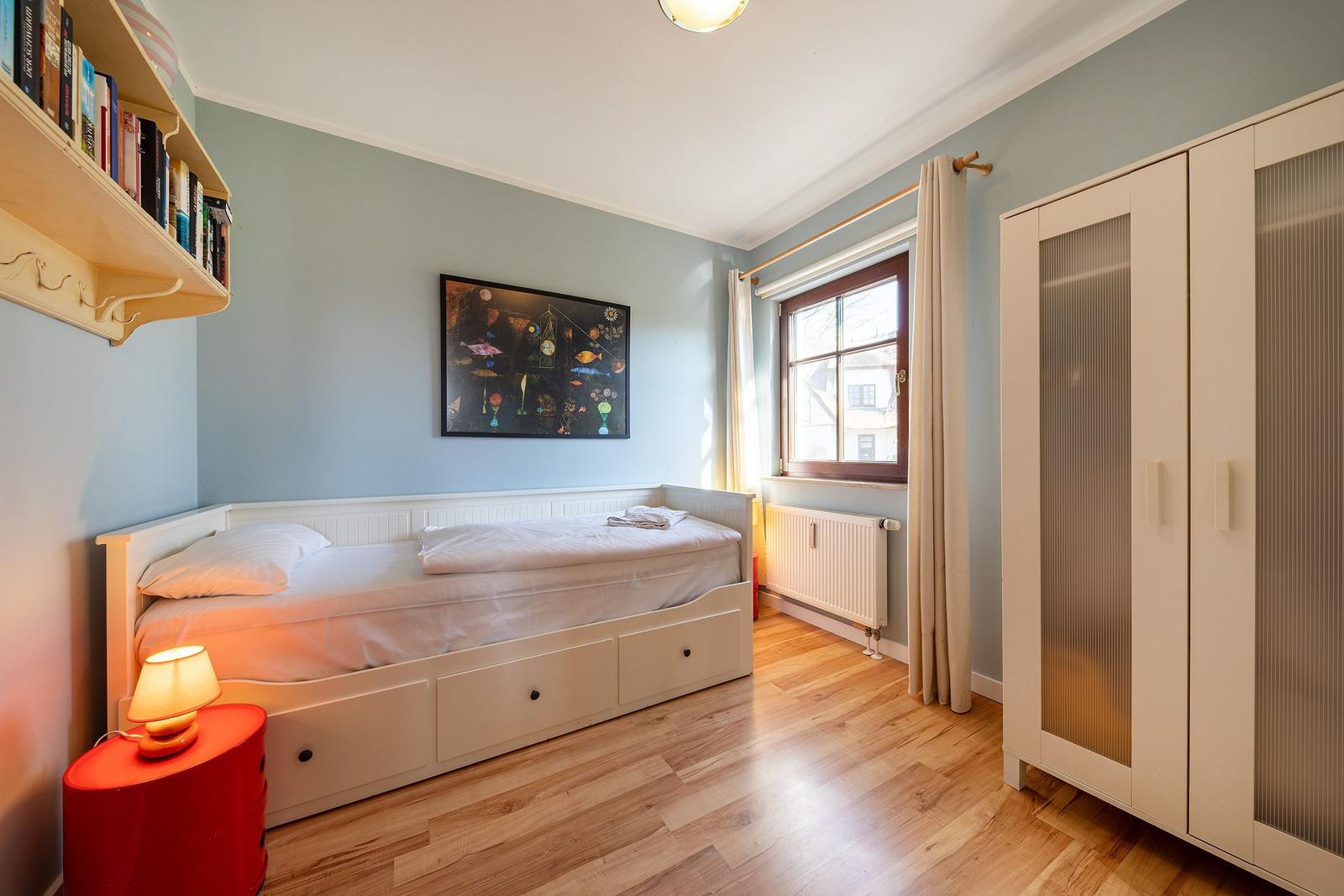 Ein Schlafzimmer mit Bett, Schrank, Fenster und Wandbild.