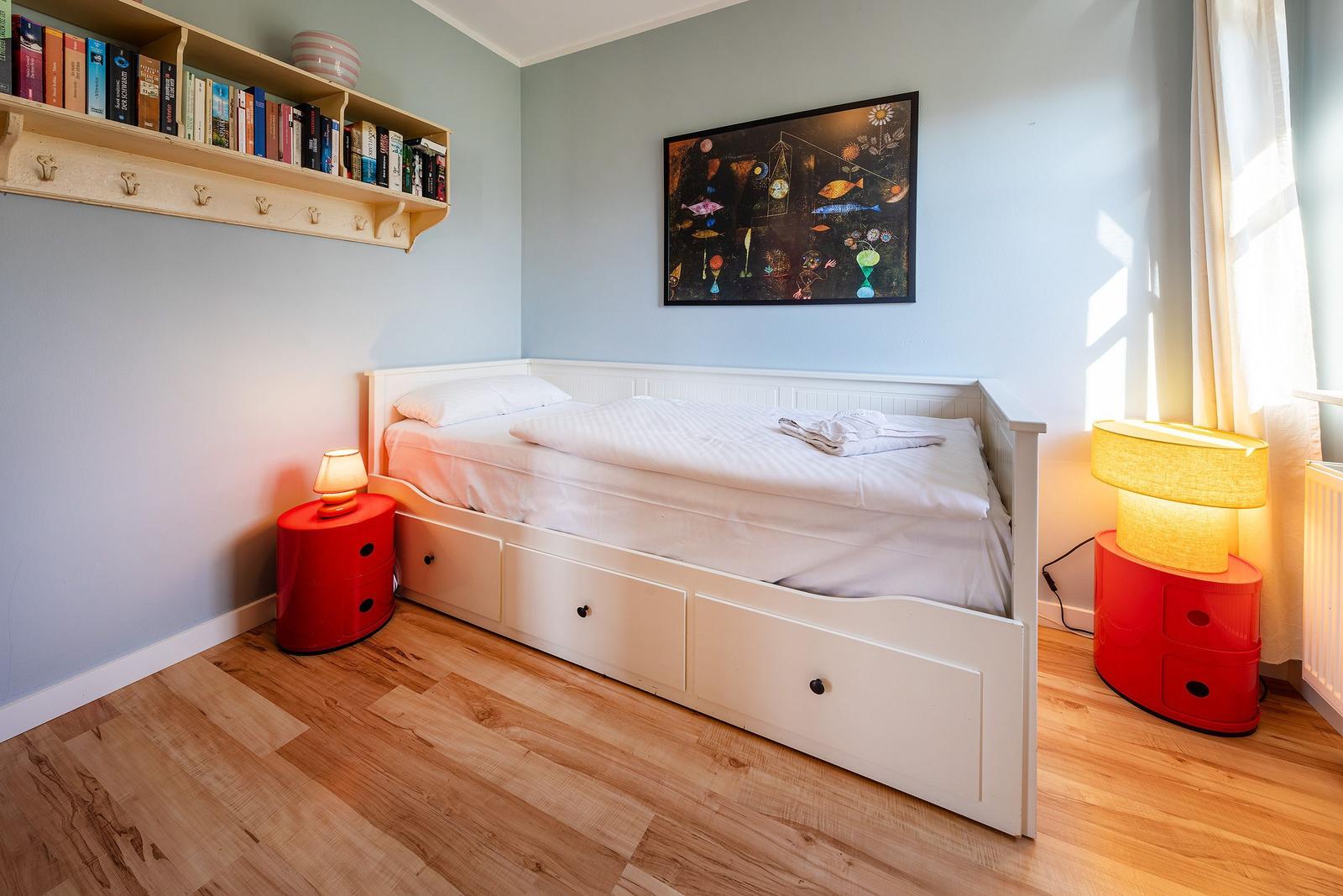 Schlafzimmer mit weißem Bett, Holzboden und roten Nachttischen.