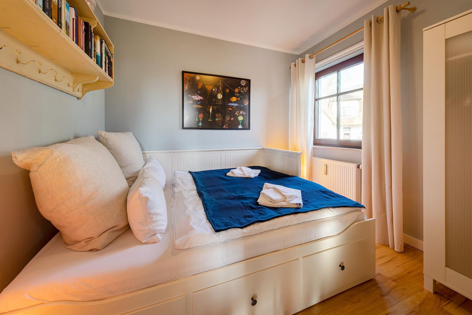 Schlafzimmer mit Bett, Bücherregal, Fenster und Kleiderschrank.