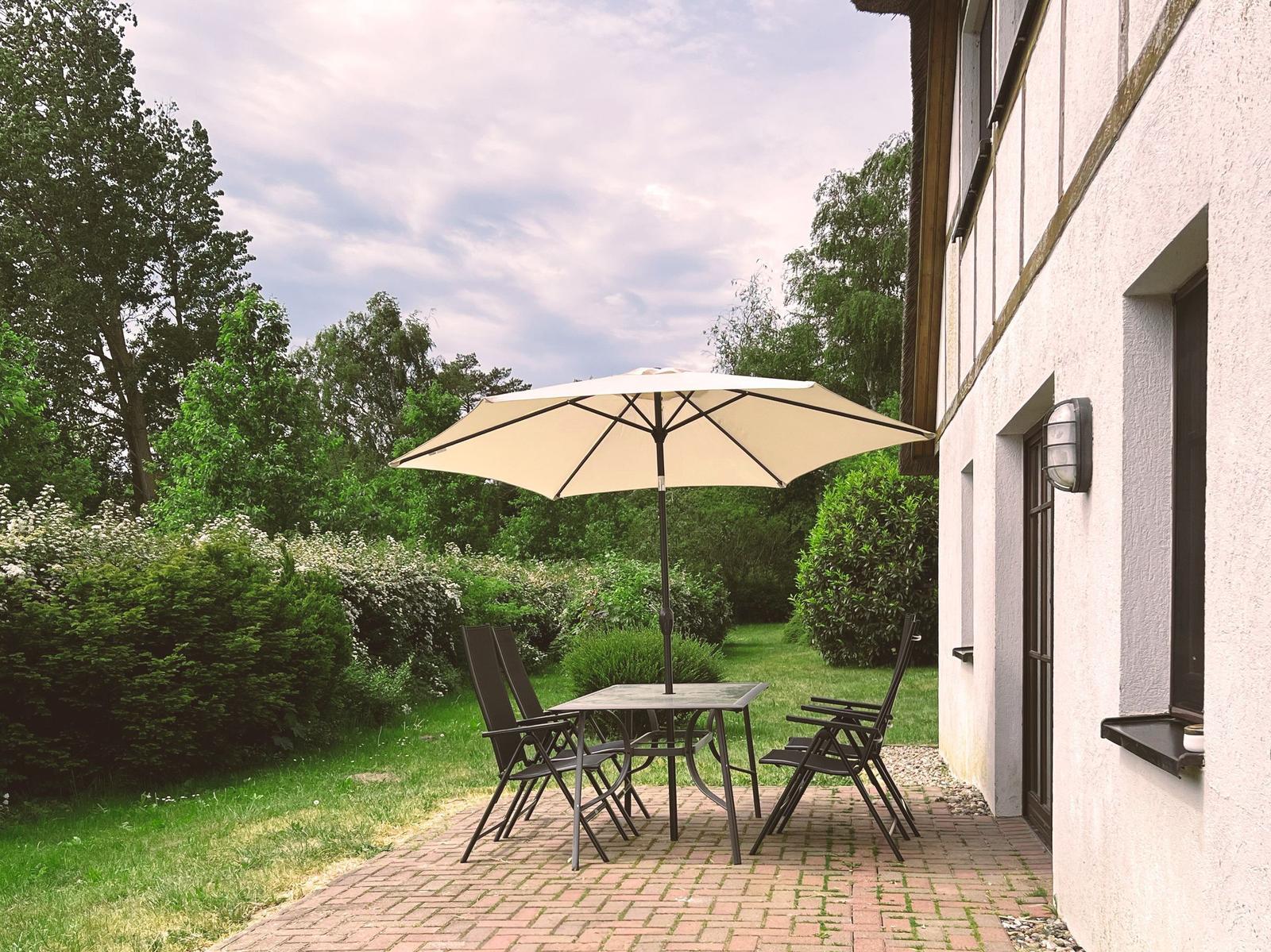 Terrasse mit Tisch, Stühlen und Sonnenschirm neben Hauswand.