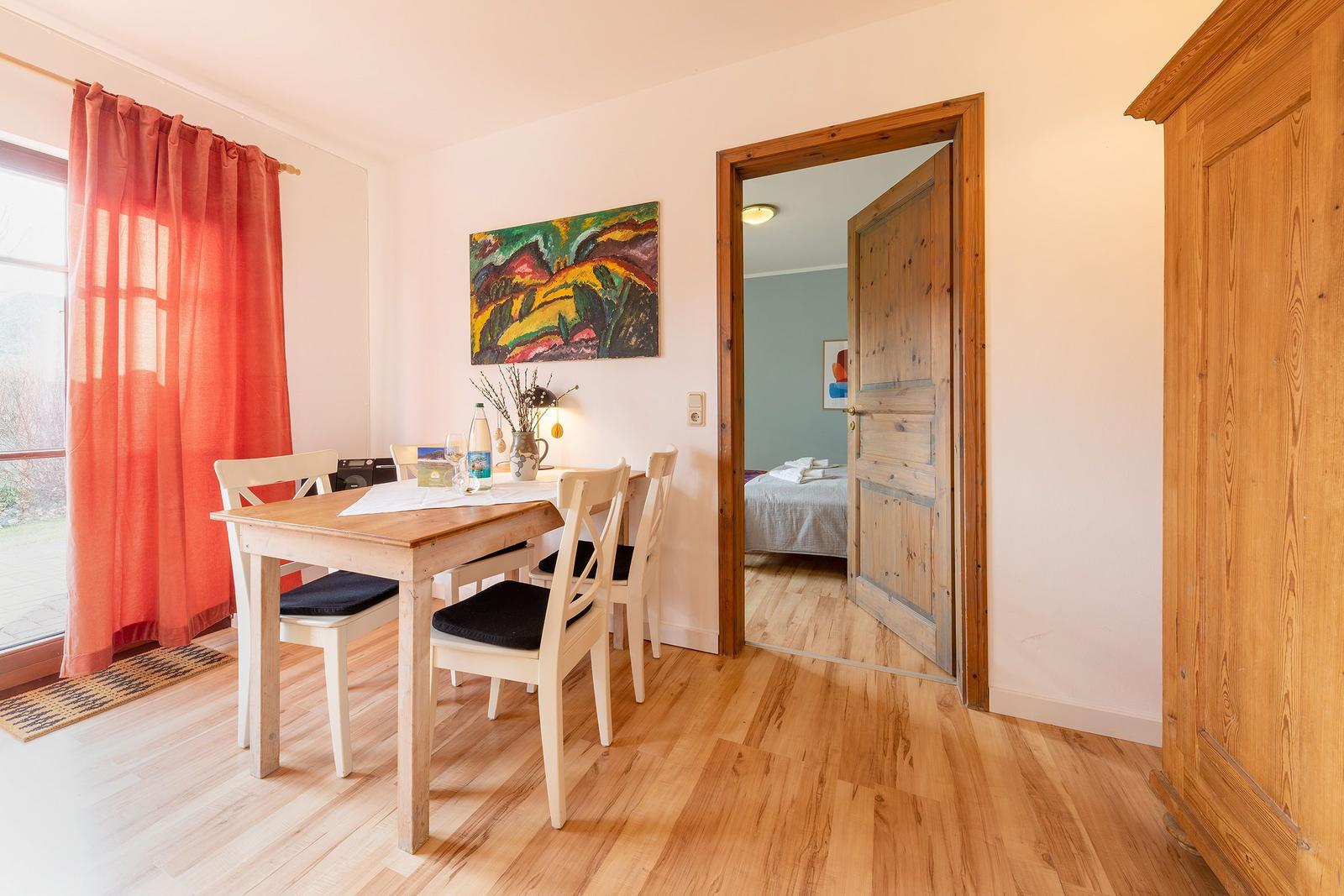 Esszimmer mit Tisch, Stühlen und Blick in Schlafzimmer. Holzfußboden und Wandbild.