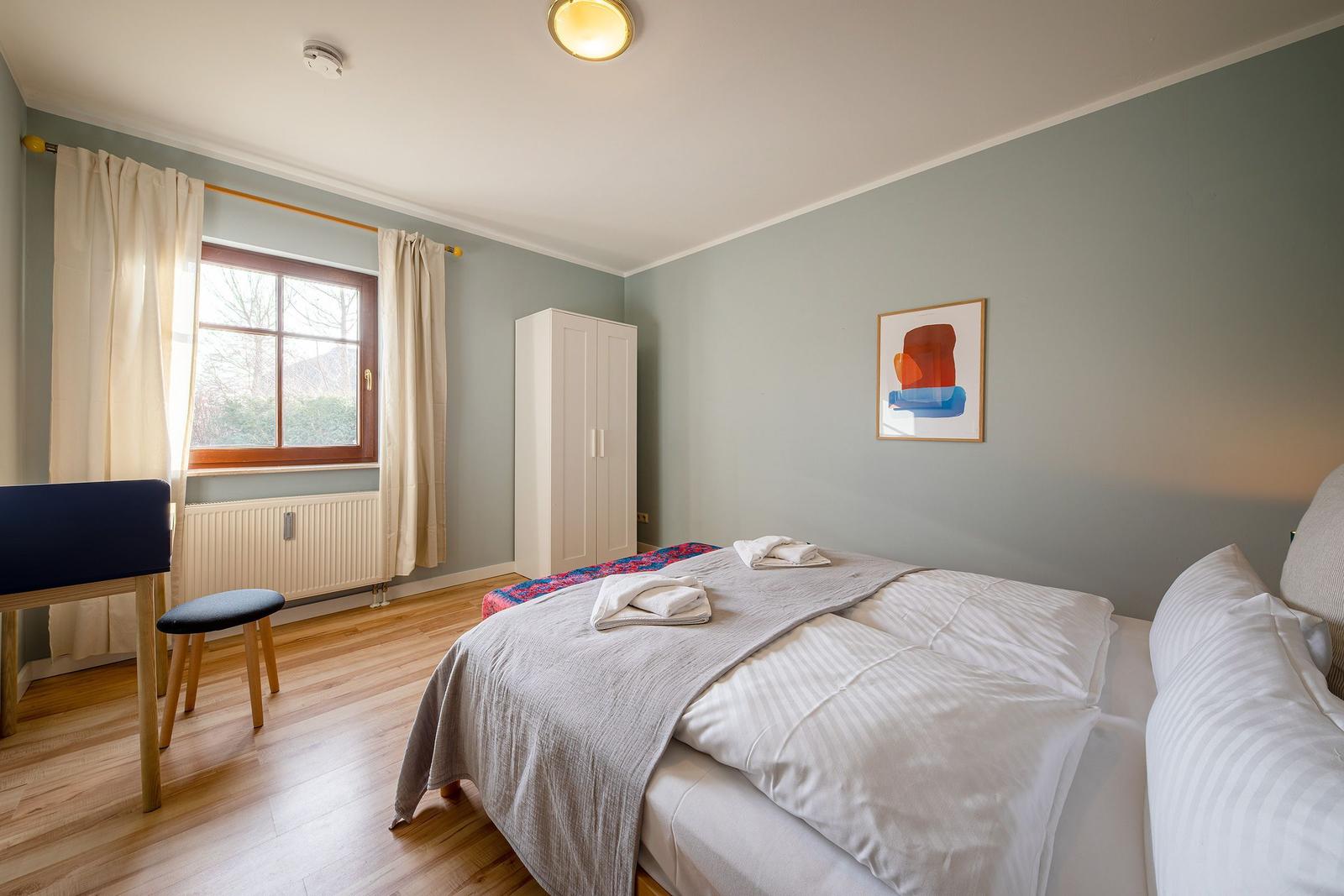 Schlafzimmer mit Bett, Kleiderschrank und Fenster mit Vorhängen.