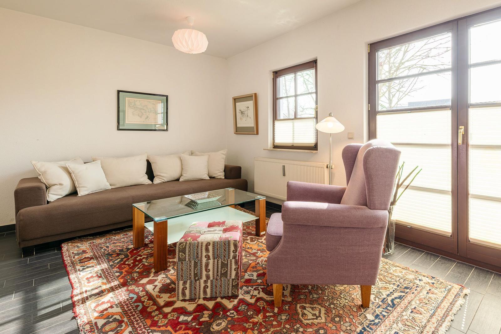 Ein Wohnzimmer mit Sofa, Sessel, Glas-Tisch und Teppich.