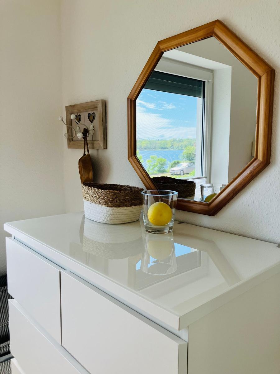 Schrank mit Spiegel, Korb und Glas mit Zitrone. Blick auf See durch Fenster.