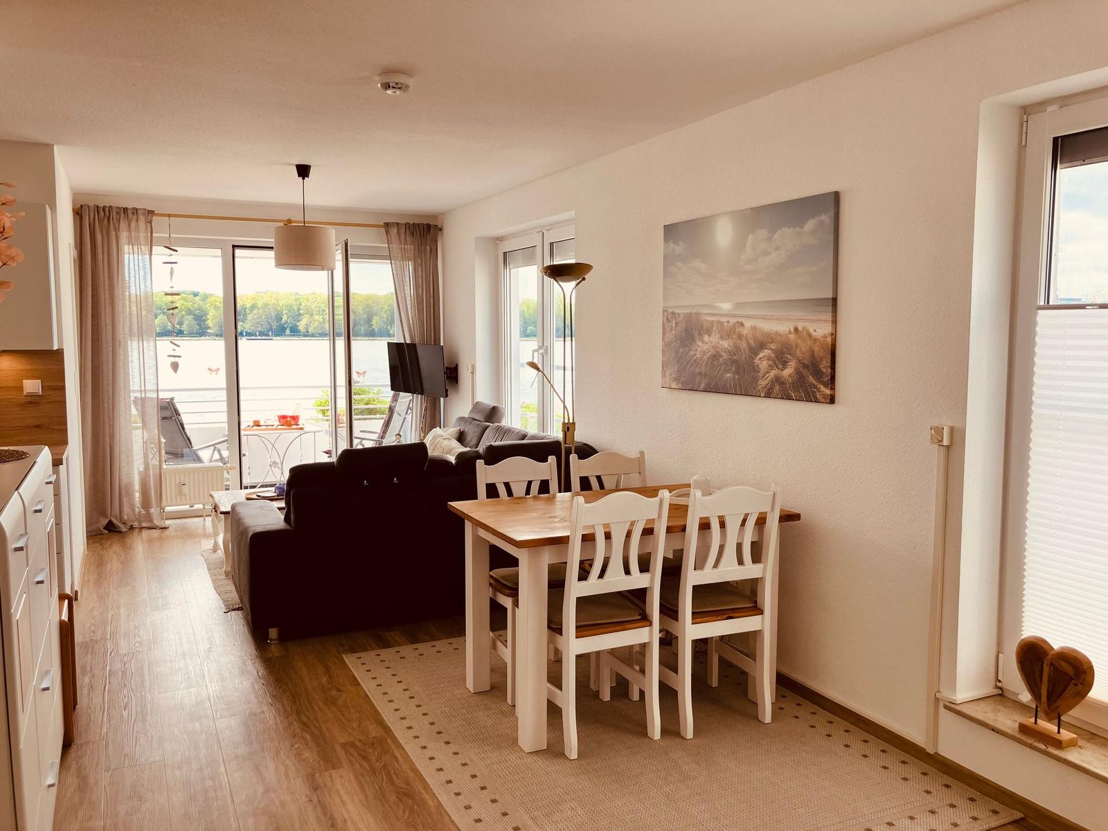 Wohn- und Essbereich mit Blick auf Wasser. Esstisch mit Stühlen und Sofa.