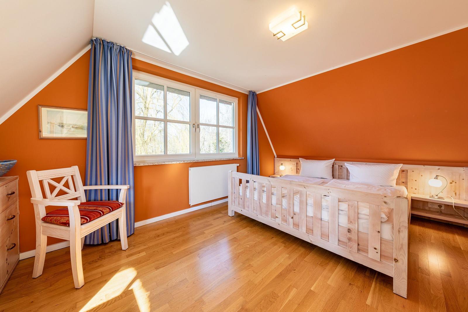Schlafzimmer mit Holzbett, Fenster, Vorhängen und Holzboden.