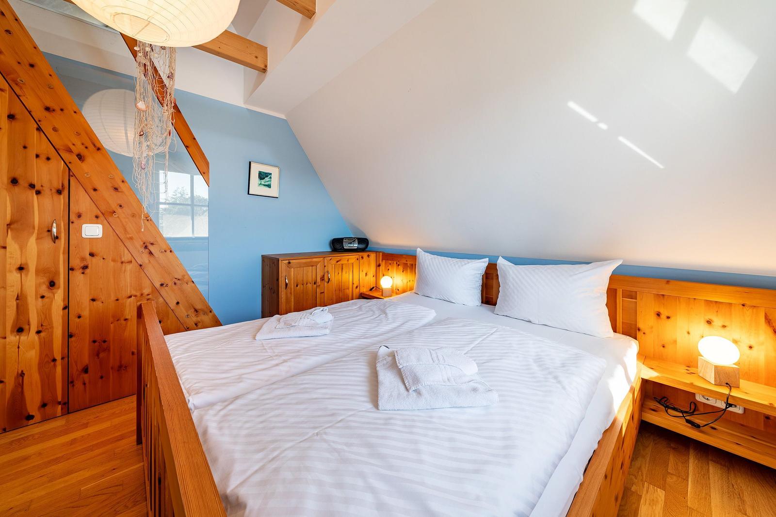 Schlafzimmer mit Doppelbett, Holzmöbel und Dachschrägen. Blaue Wand und Fenster.