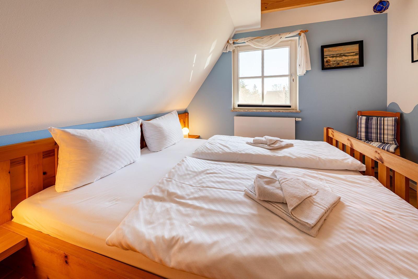 Zimmer mit Doppelbett, Fenster und Holzmöbel.