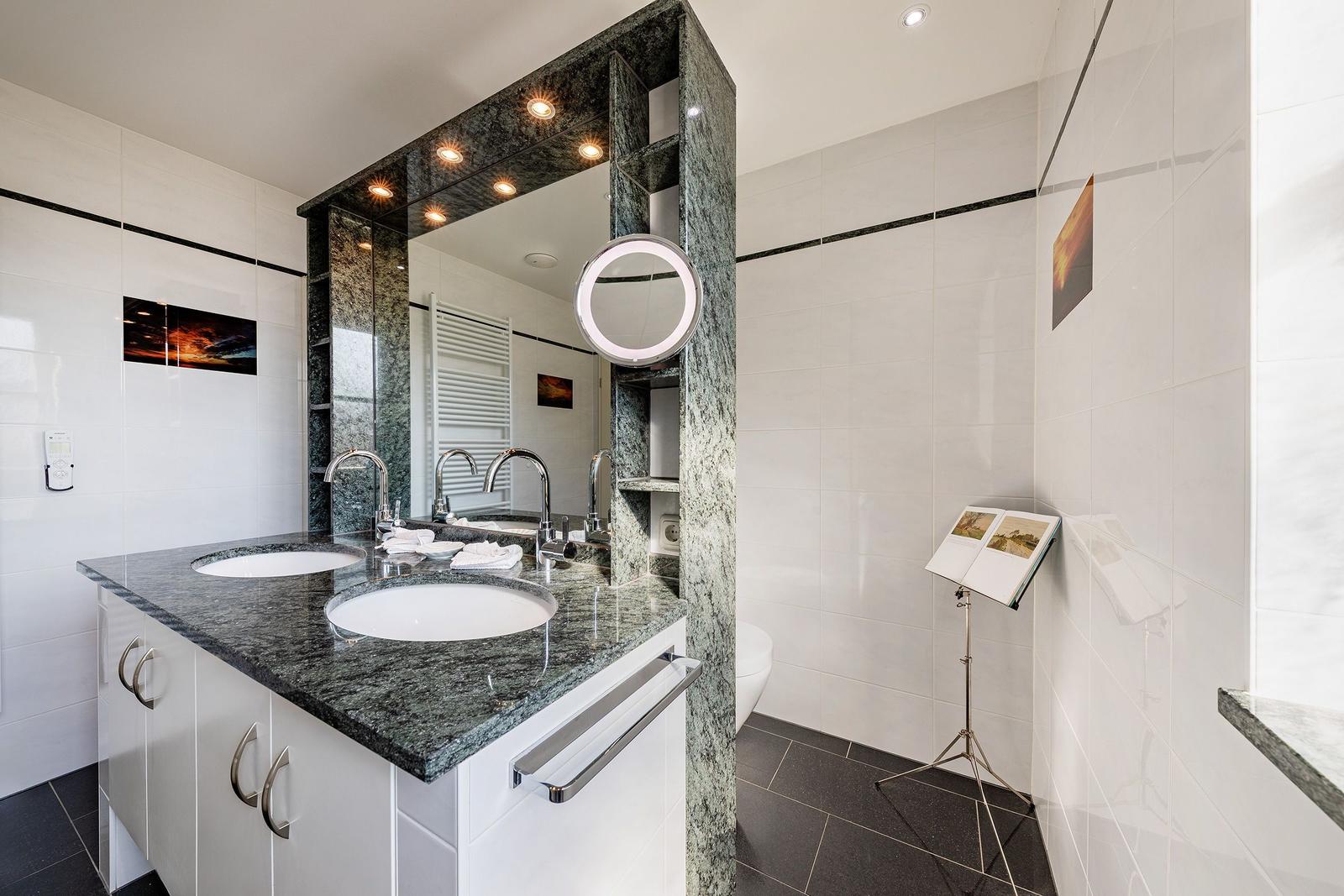 Doppelwaschbecken mit dunklem Marmor, Spiegelschrank und runden Spiegel.