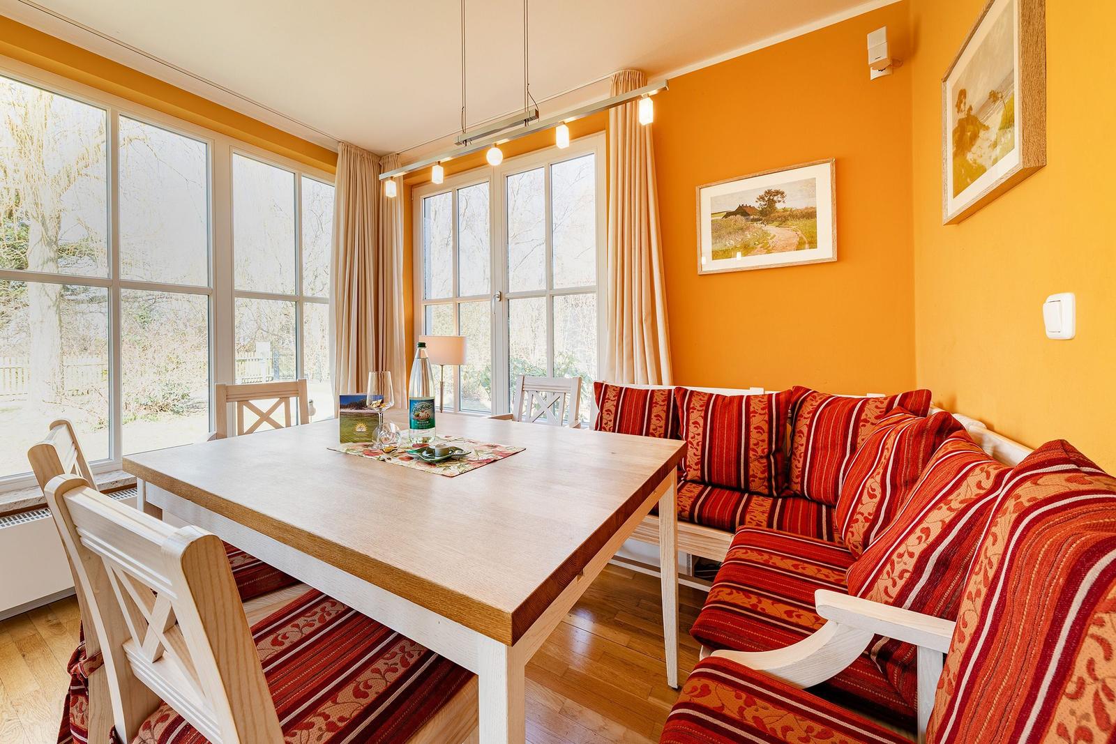 Esszimmer mit Holztisch, Sitzbank und Fenstern. Wandfarbe orange.