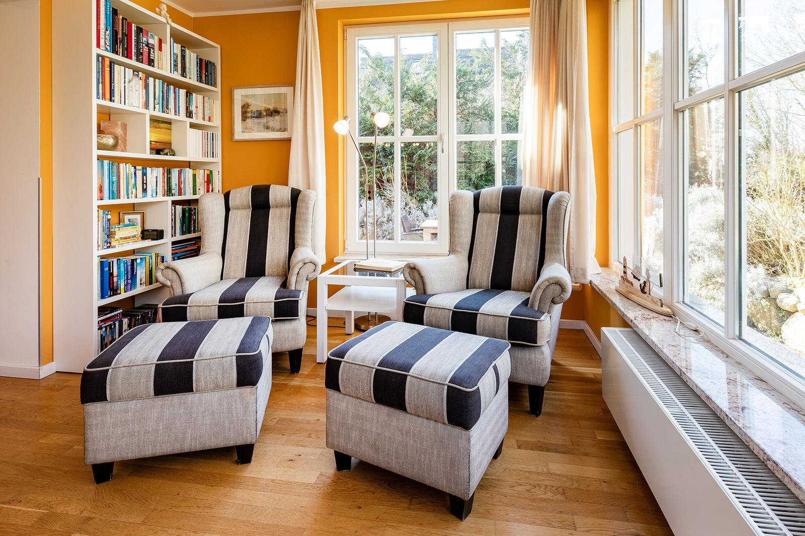 Zwei Sessel mit Füßen und ein Bücherregal an der Wand.