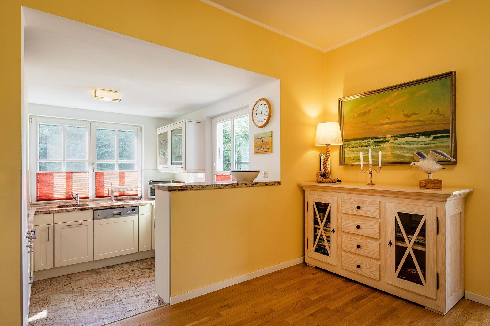 Küche mit Arbeitsplatte und Fenster. Wohnbereich mit Sideboard und Wandbild.