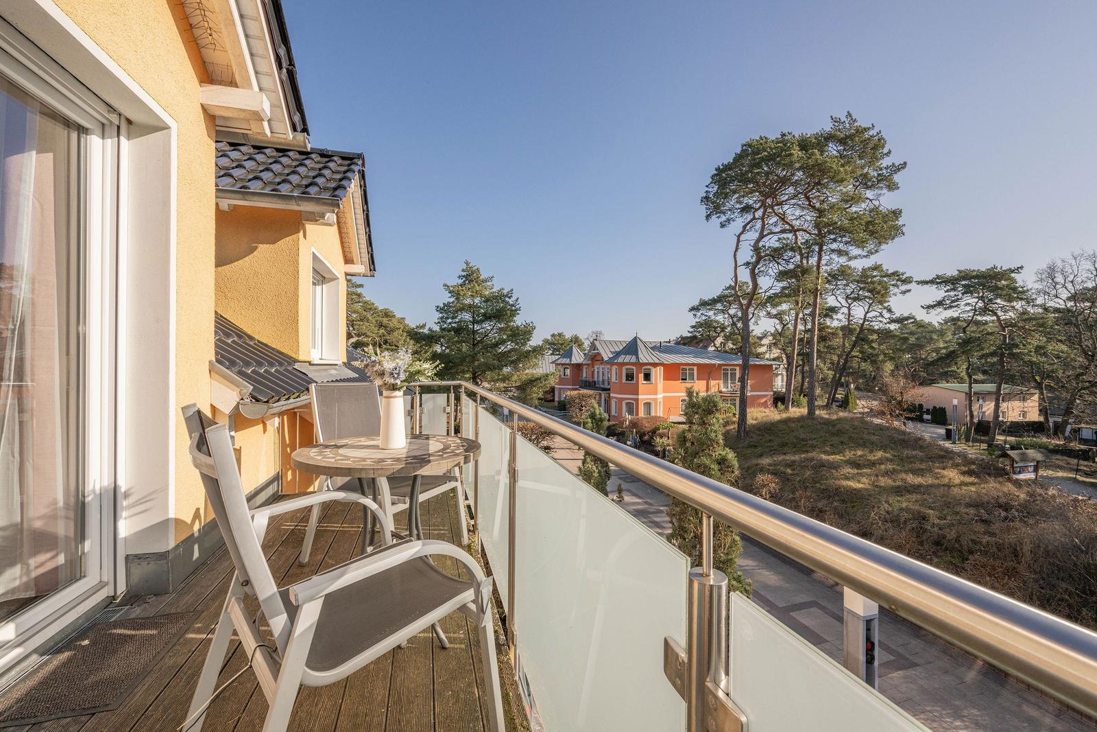 Balkon mit Tisch und Stühlen, Blick auf grüne Bäume und ein orangefarbenes Haus.