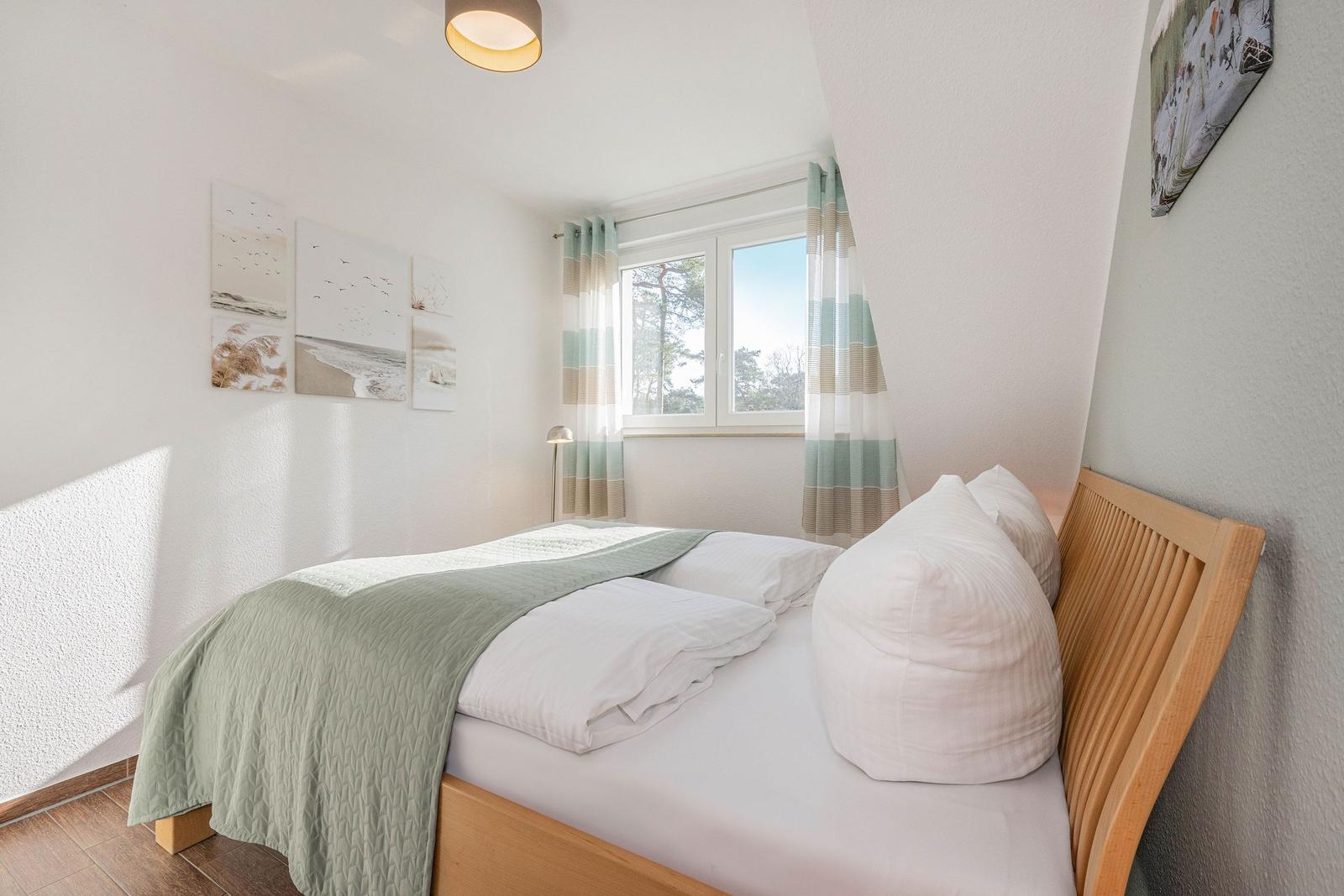 Schlafzimmer mit Doppelbett, Fenster und Wandbildern.