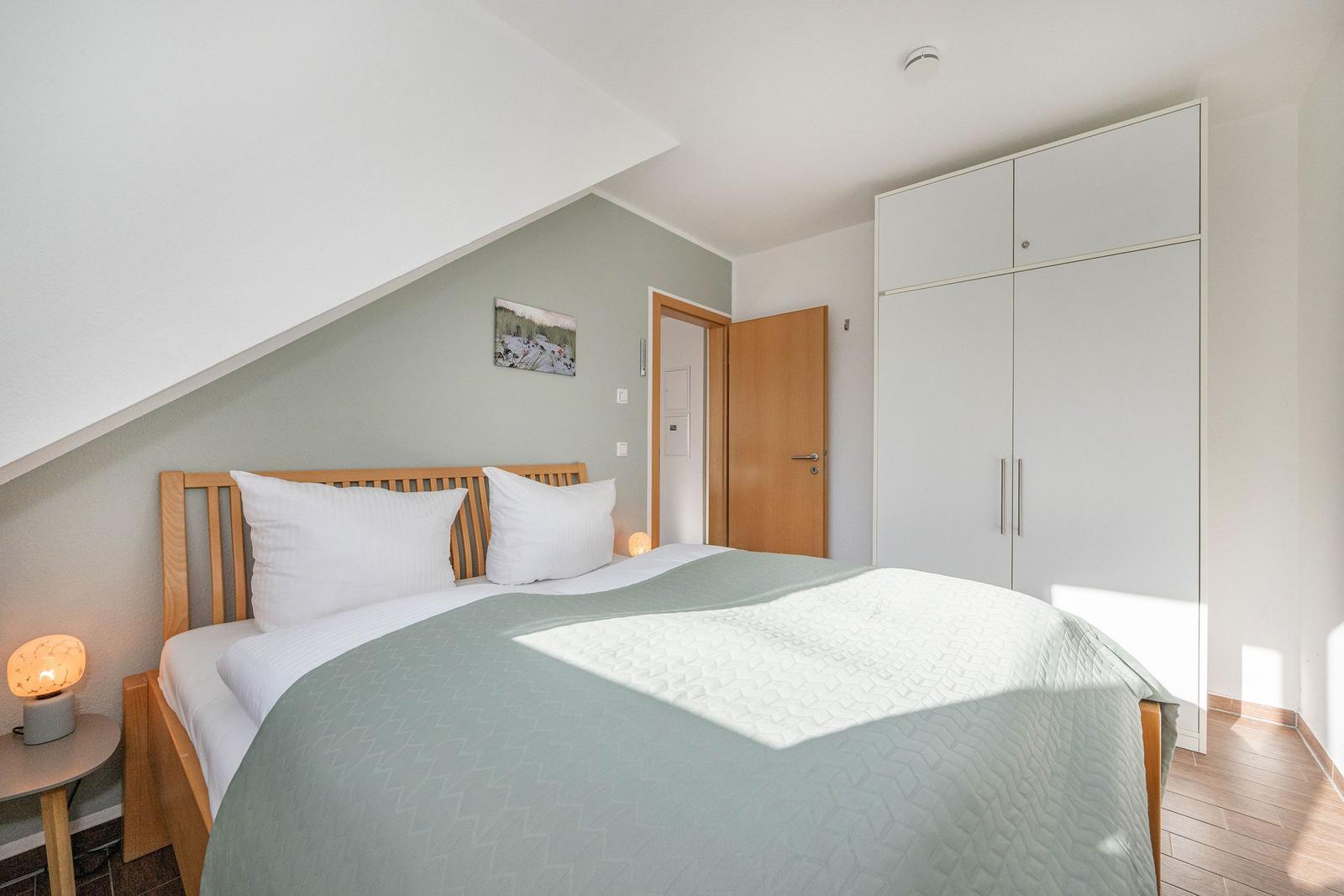 Schlafzimmer mit Bett, Kleiderschrank und Nachttisch unter schräger Decke.