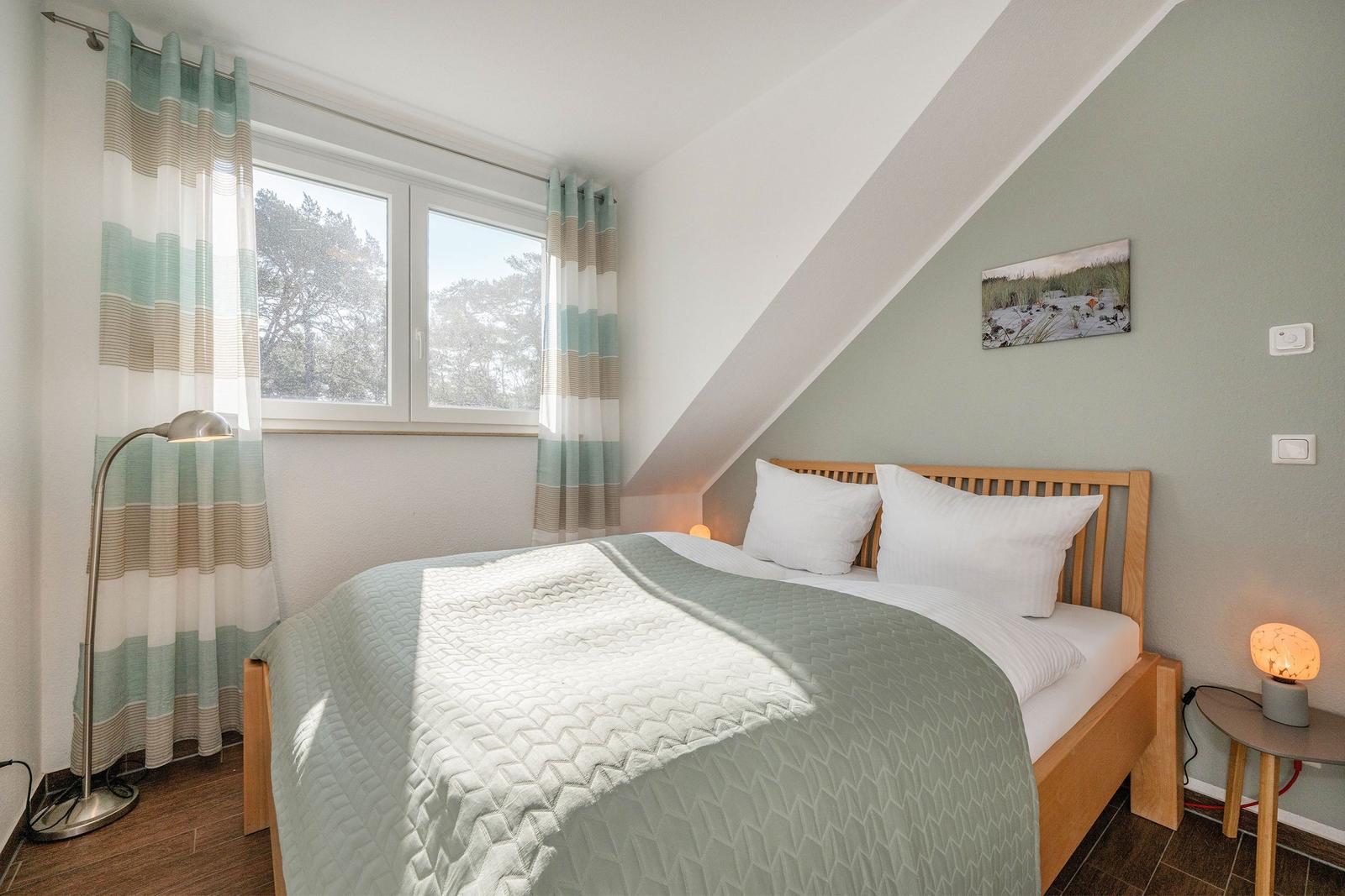 Schlafzimmer mit Dachschrägen, Bett, Fenster und Gardinen.