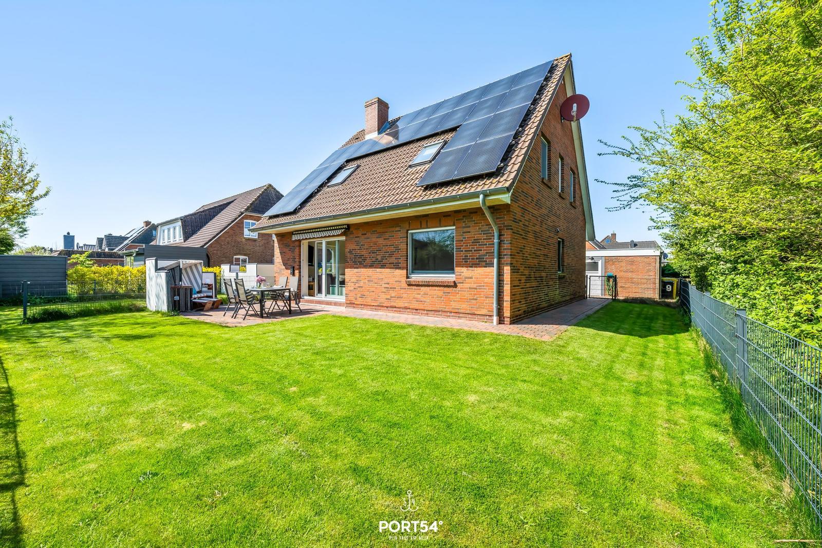 Ein Haus mit Solarpanelen auf dem Dach und einem großen Garten mit Terrasse.