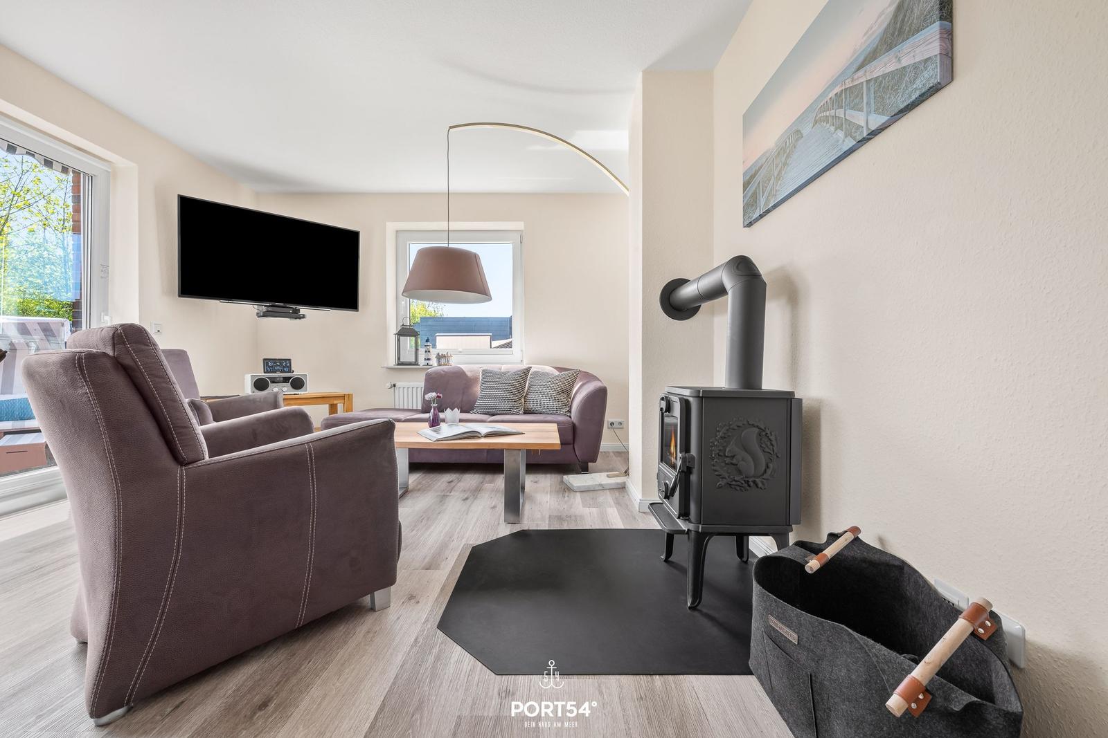 Wohnzimmer mit Sitzgelegenheiten, Kaminofen und Fernseher an der Wand.