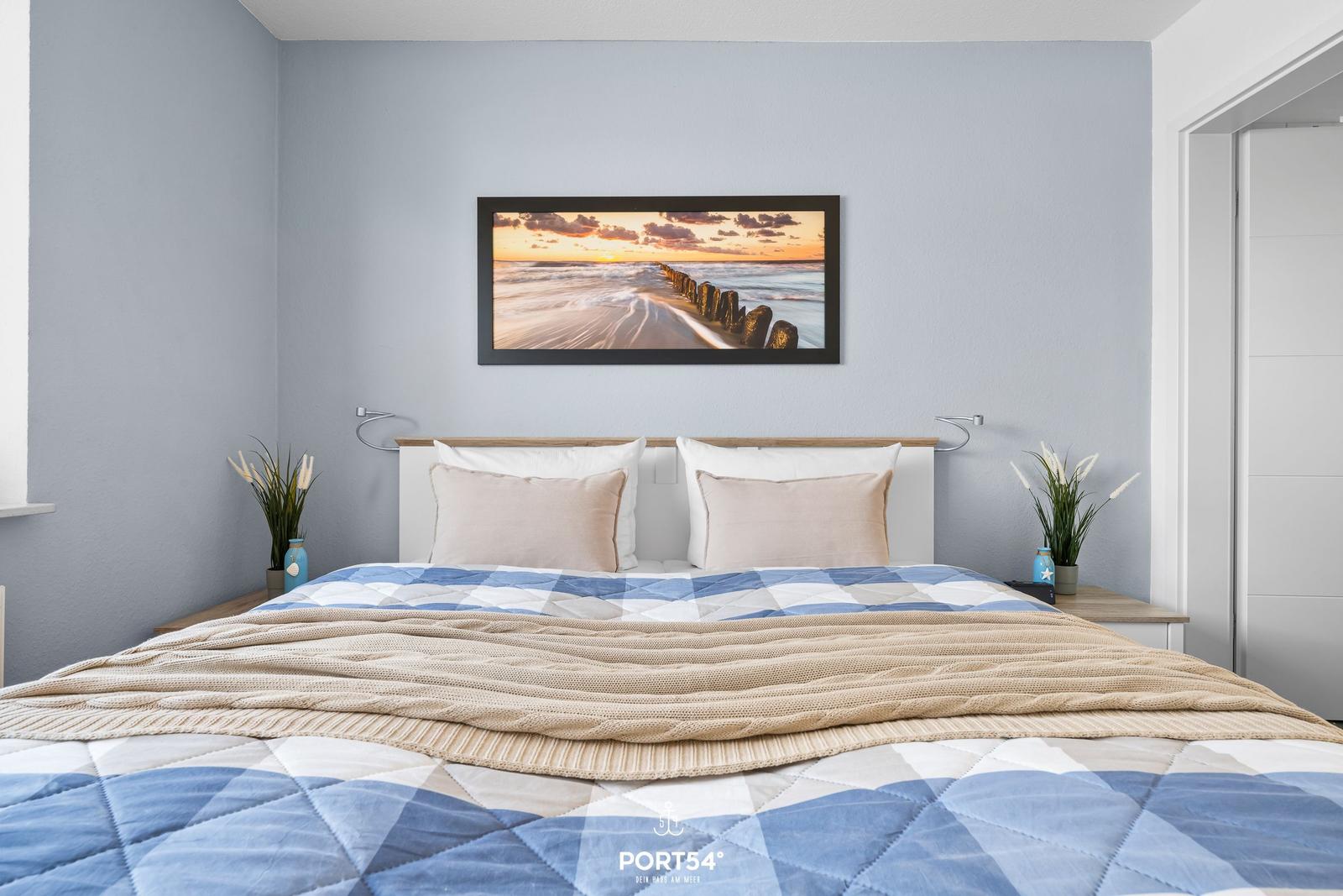 Schlafzimmer mit Bett, Wandbild und Nachttischen.
