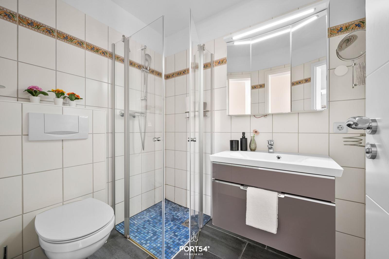 Bad mit Dusche, Waschbecken und Toilette. Fliesen und Spiegel sind sichtbar.