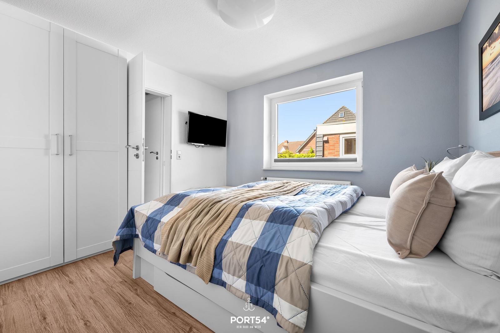 Schlafzimmer mit Bett, Kleiderschrank und Fenster zum Hausblick.