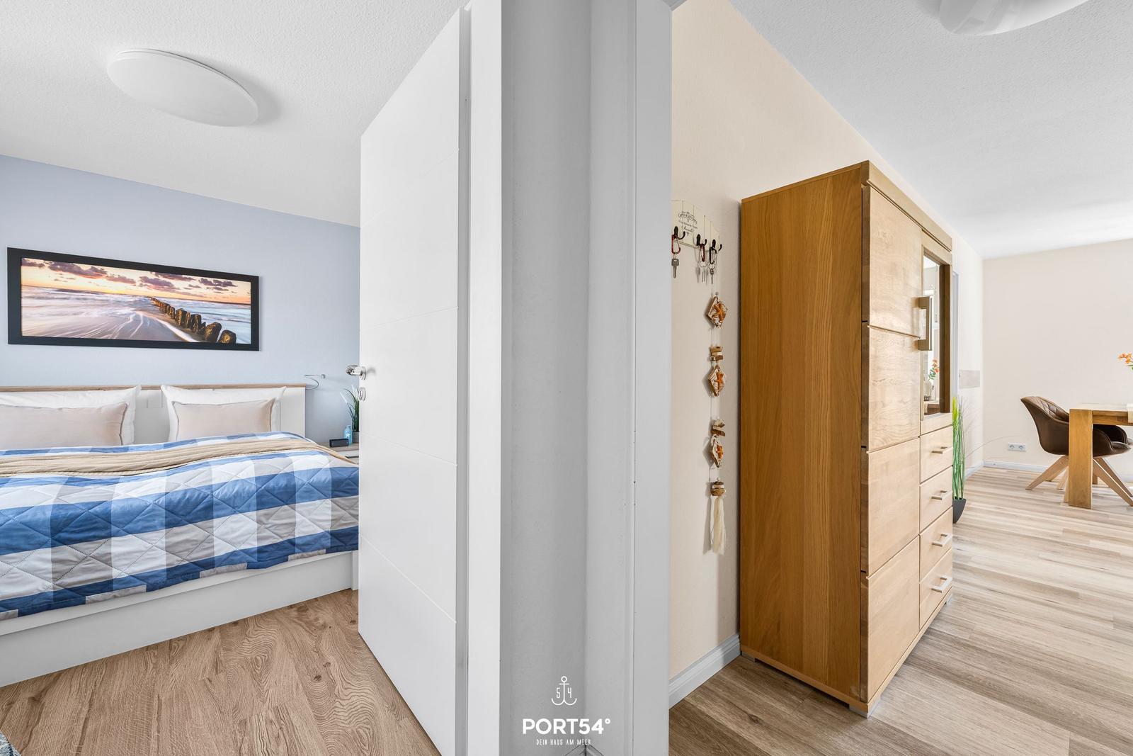 Schlafzimmer mit Bett und Wandbild. Flur mit Kleiderschrank und Tisch.