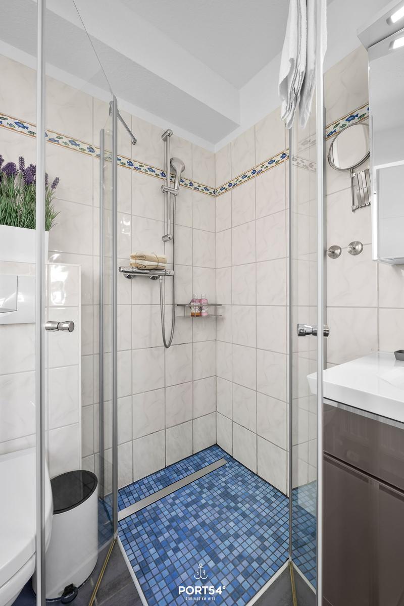 Dusche mit Glaswand, blauem Mosaikboden und weißen Fliesen.